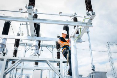 Koruyucu kasklı elektrikçi yüksek voltajlı elektrik hatları üzerinde çalışıyor. Elektrik şebekesine hizmet eden çok yetenekli işçiler. Güç kuleleri olan modern enerji santrali