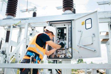 Koruyucu kasklı elektrikçi yüksek voltajlı elektrik hatları üzerinde çalışıyor. Elektrik şebekesine hizmet eden çok yetenekli işçiler. Güç kuleleri olan modern enerji santrali