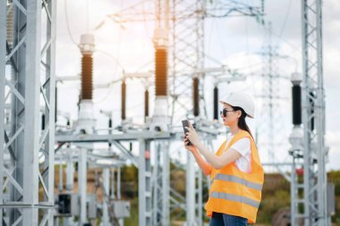 Yetişkin kadın enerji mühendisi tabletteki verileri kullanarak modern güç istasyonunun ekipmanlarını inceliyor. Güç mühendisliği.