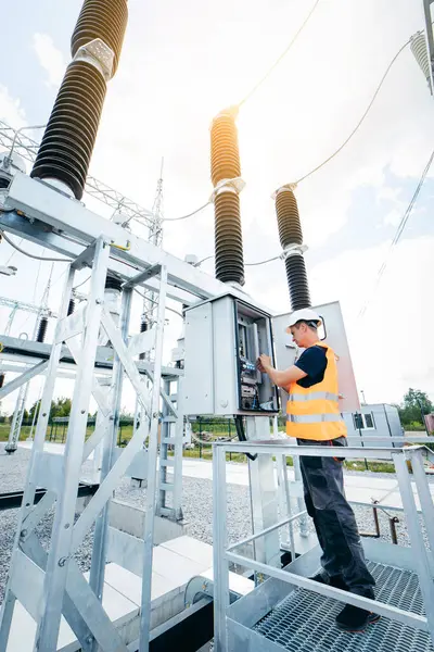 Koruyucu kasklı elektrikçi yüksek voltajlı elektrik hatları üzerinde çalışıyor. Elektrik şebekesine hizmet eden çok yetenekli işçiler. Güç kuleleri olan modern enerji santrali