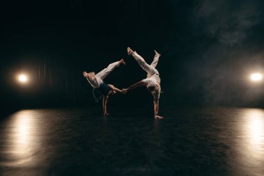 Siyah arka planda Capoeira eğitimi alan iki savaşçı.