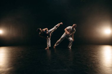 Siyah arka planda Capoeira eğitimi alan iki savaşçı.