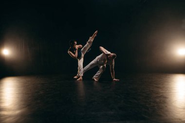 Siyah arka planda Capoeira eğitimi alan iki savaşçı.
