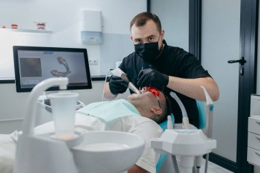Dişçi, erkek hastanın dişlerini modern 3D tarama makinesiyle tarıyor.