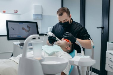 Dişçi, erkek hastanın dişlerini modern 3D tarama makinesiyle tarıyor.