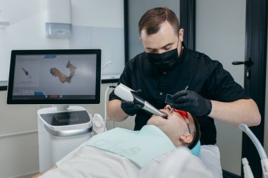 Dişçi, erkek hastanın dişlerini modern 3D tarama makinesiyle tarıyor.