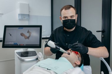 Dişçi, erkek hastanın dişlerini modern 3D tarama makinesiyle tarıyor.
