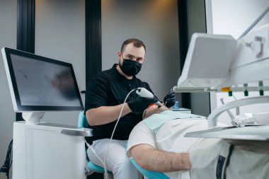 Dişçi, erkek hastanın dişlerini modern 3D tarama makinesiyle tarıyor.