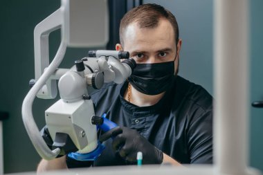 Erkek dişçi modern mikroskopla hastanın dişlerini inceliyor.