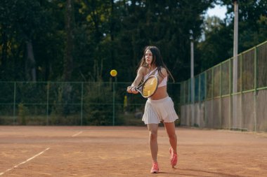 Genç bir kadın yazın dışarıda tenis oynuyor.