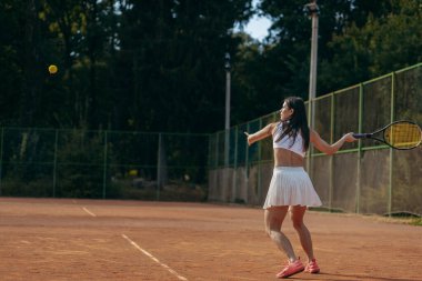 Genç bir kadın yazın dışarıda tenis oynuyor.