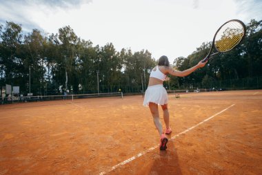 Genç bir kadın yazın dışarıda tenis oynuyor.