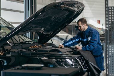 Otomobil tamircisi kaputun altındaki lüks arabayı inceliyor.