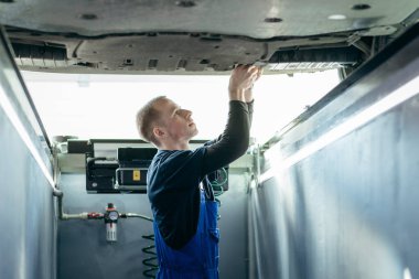 A car mechanic adjusts wheels in a car repair shop clipart