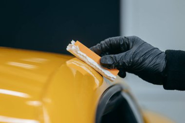 Araba temizleme işçisi atölyedeki sarı arabanın üzerine seramik araba sürüyor.