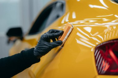 Araba temizleme işçisi atölyedeki sarı arabanın üzerine seramik araba sürüyor.