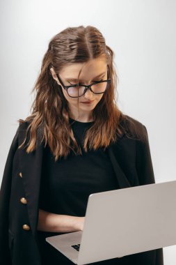 Siyah takım elbiseli başarılı genç bir iş kadını stüdyoda bilgisayarla beyaz arka planda çalışıyor.