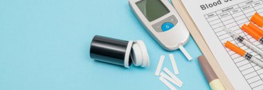 Glukometre ve insülin şırıngası, kesici alet test şeridi. Mavi arkaplanda.