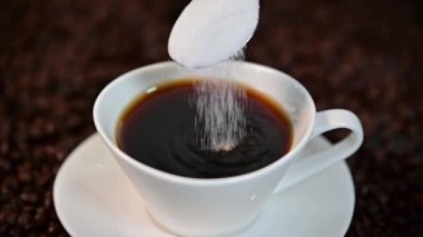 a Spoon of white sugar pouring into a cup full of black coffee in slow motion