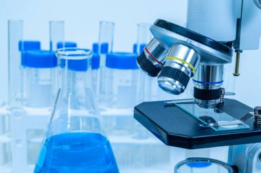 Mavi sıvı erlenmeyer matarası ve mikroskop yakın plan.