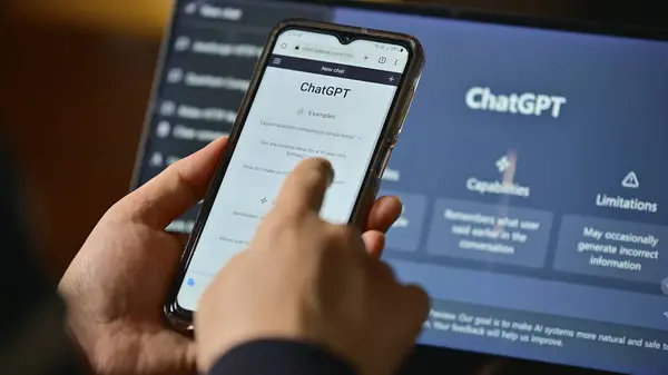 Seoul, South Korea - February, 2023 : Computer screen with ChatGPT website and person using mobile phone to ask questions to ChatGPT