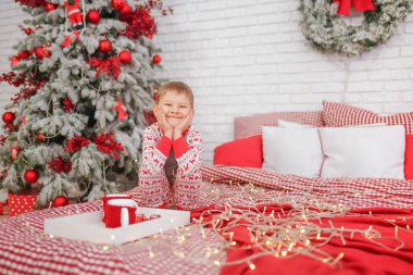Yatakta yeni yıl pijamaları giymiş bir çocuk elinde sıcak kakao bardaklarıyla Noel 'i bekliyor. Yaşam tarzı. mesaj için yer. Yüksek kalite fotoğraf