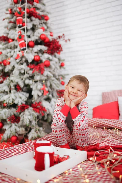 Yatakta yeni yıl pijamaları giymiş bir çocuk elinde sıcak kakao bardaklarıyla Noel 'i bekliyor. Yaşam tarzı. mesaj için yer. Yüksek kalite fotoğraf