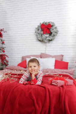 Avrupalı çocuk yeni yıl tatilini bekliyor. Yüzünde hüzünlü bir ifadeyle yatağında kırmızı tonlarda yatıyor. Duygular, bayram arifesindeki çocuğun ruh hali.