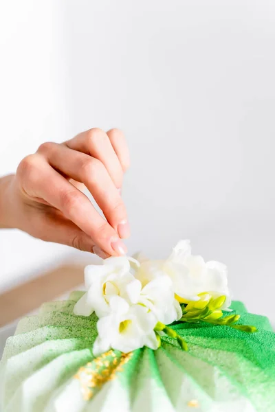 A close-up of a mousse cake on a white background, and a strong hand fixes white flowers on the cake. confectioner concept