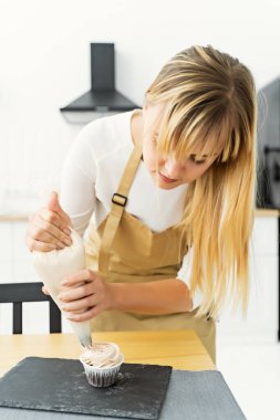 Decorate the cake with white cream. Using a pastry bag, the pastry chef makes cupcakes. Shot of female hands applying butter cream on delicious cakes, homemade pastries