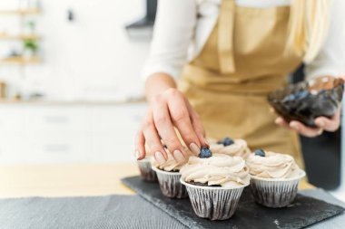 Women's hands of a confectioner, decorating cupcakeswith blueberries and chocolate. Close-up, space for text