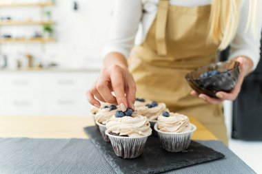 Women's hands of a confectioner, decorating cupcakeswith blueberries and chocolate. Close-up, space for text