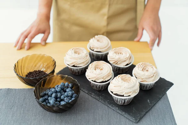 Confectioner decorating cupcake with blueberry. Cooking class, culinary and bakery. Desserts. Confectioner decorate cupcakes with cream cheese, close up. Homemade pastry. Woman cooking cakes