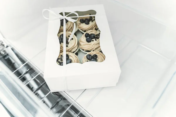 Delicious little cupcakes in the fridge, packaged in a cardboard box. Fresh sweet pastry for coffee break. Chocolate brownies in the freezer