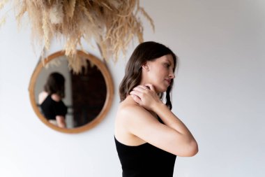 Siyah elbiseli kahverengi saçlı bir kadın elini boynundan tutuyor. Sağlık sorunları, boyun ağrısı.