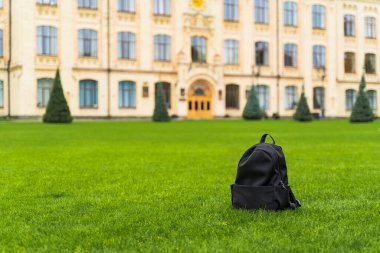 Üniversite ve okulun arka planında yeşil çimlerin üzerinde duran siyah bir okul çantası. Yüksek kalite fotoğraf