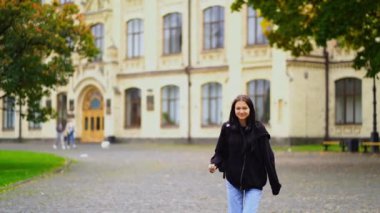 Genç neşeli esmer öğrenci kampüsün yakınında ağır çekimde zıplıyor. Öğrenci hayatı, sınavlar. Yüksek kaliteli FullHD görüntüler