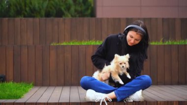Genç bir kız ahşap bir bankta oturmuş köpeğini okşuyor. Yüksek kaliteli FullHD görüntüler
