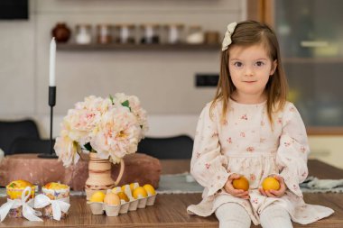 A girl in a white cloth is sitting in the kitchen and holding Easter eggs in her hands. Holy, traditions, Easter. High quality photo clipart