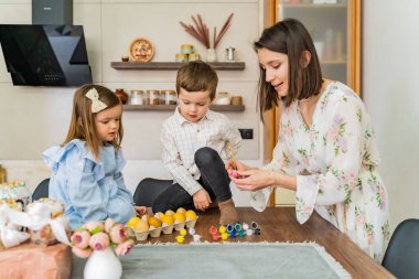 Paskalya aile gelenekleri. Paskalya bayramında süslemeleri için çocukların resimlerini hazırlayan, mutfak masasında yan yana oturan genç bir anne. Yüksek kalite fotoğraf