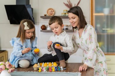Bir erkek ve bir kız, annelerinin yanındaki mutfakta paskalya yumurtası boyuyor. Yüksek kalite fotoğraf