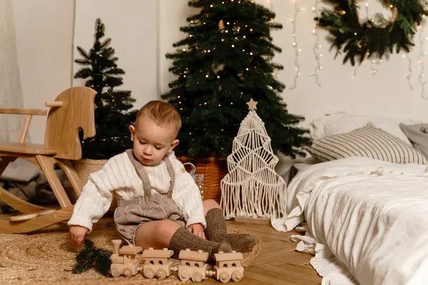 Küçük bir çocuk Noel ağacının yanında oturur ve bir köy treniyle oynar. Yüksek kalite fotoğraf
