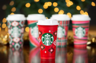 Dallas, Teksas - 18 Kasım 2023: yeni tasarlanmış tatil bardaklarında Starbucks kahvesi. Ön tarafta yeniden kullanılabilir kırmızı bardak ve arka planda da tek kullanımlık kağıt bardak. Noel Bokeh 'ine Karşı Gösterilen.