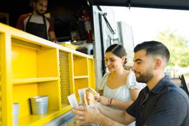 Çekici, neşeli kadın ve adam fast food kamyonundan lezzetli bir sandviç yiyorlar.