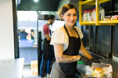 Fast food kamyonunda aşçı olarak çalışan çekici genç bir kadın sandviç hazırlıyor.
