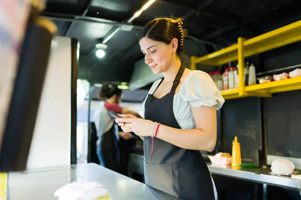 食品トラックで女性の屋台ベンダーは スマートフォン上の配信アプリ上で顧客の注文をチェック — ストック写真