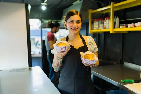 Beautiful food truck worker smiling while serving sandwiches orders to diners