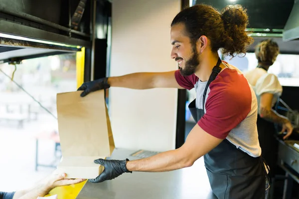 食品注文で顧客に配達袋を与える魅力的なラテンフードトラックの労働者 — ストック写真