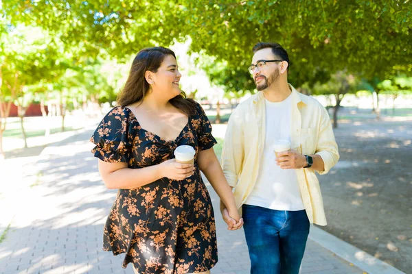 公園で手を取りながらコーヒーを飲みながら笑って興奮している陽気な笑顔のカップル — ストック写真