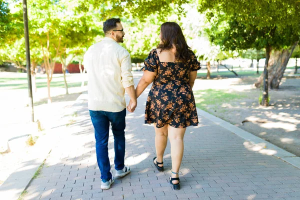 若いです男のリアビュー日付太ったラテン女性が一緒に公園でデート中に手を取り合って歩く — ストック写真
